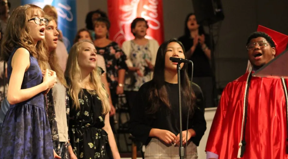 Studenti della Northside Christian Academy si esibiscono su un palco con un sipario rosso e cantano insieme.