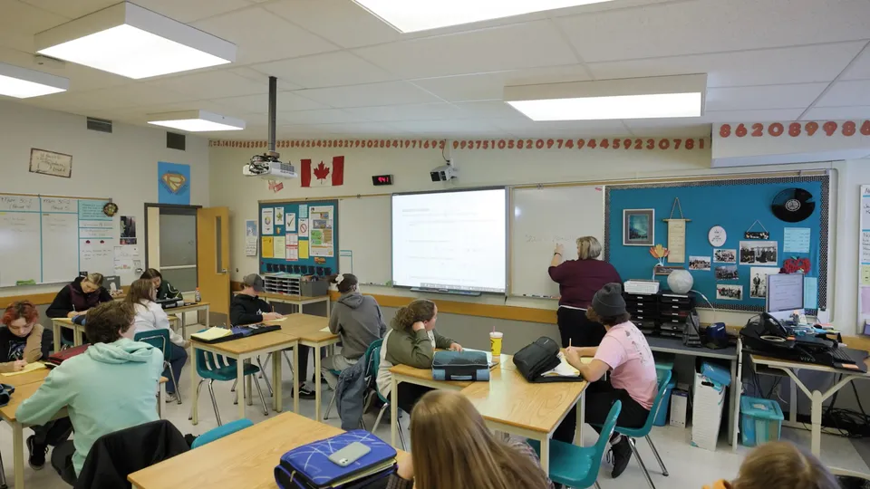 Studenti seduti ai banchi in un'aula della Eagle Butte High School mentre un'insegnante scrive sulla lavagna.
