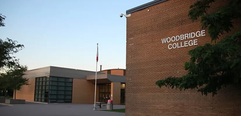 L'edificio in mattoni con la scritta Woodbridge College è circondato da alberi e da un'area pavimentata.
