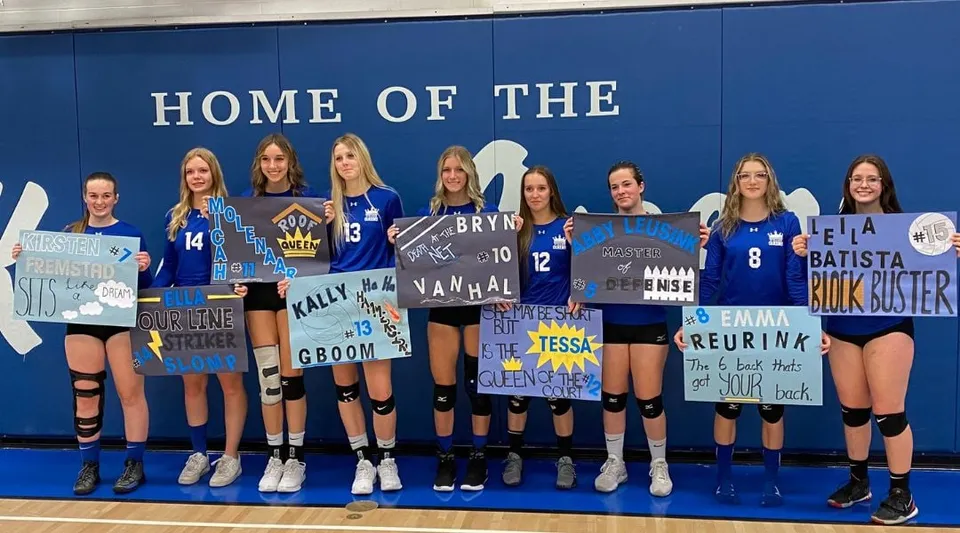 Un gruppo di giocatrici di pallavolo posa davanti a una parete blu nel campus della Picture Butte High School.