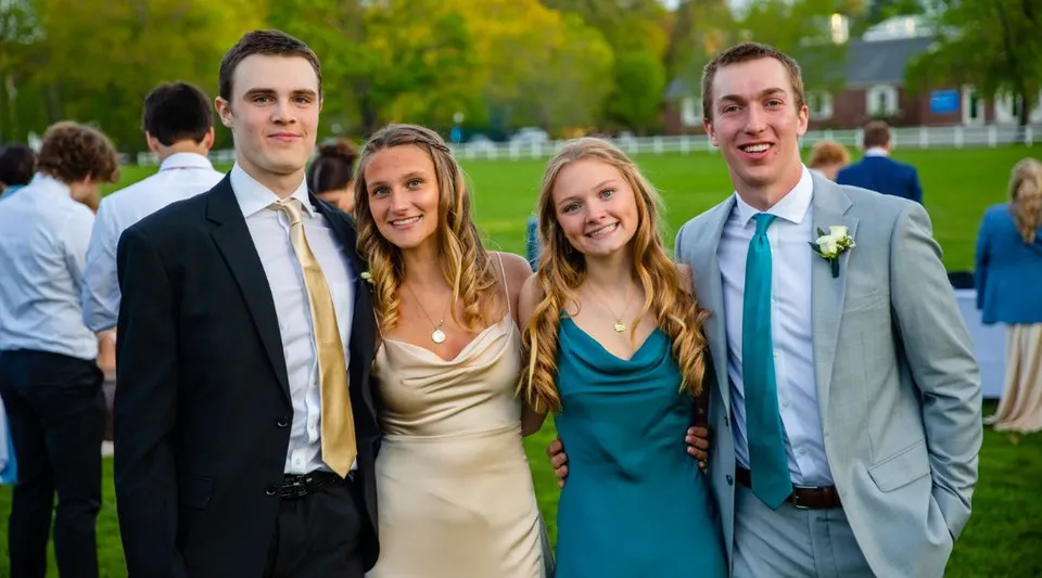 Quattro studenti della Holderness School in posa insieme all'aperto in abiti eleganti, davanti ad alberi e un prato.