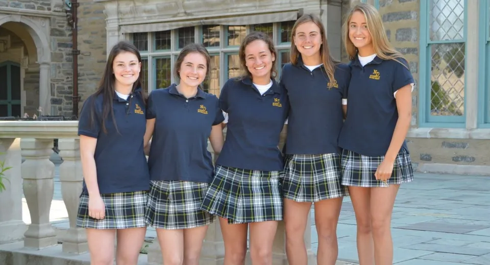 Un gruppo di cinque studentesse in divisa scolastica si trova davanti a un edificio in pietra della Academy of Notre Dame.