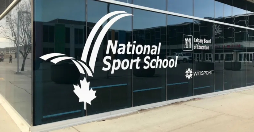 L'edificio moderno in vetro della National Sport School con una grande scritta e il logo della foglia d'acero visto dall'esterno.