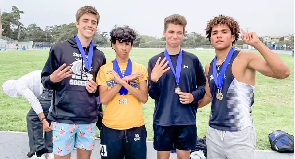 Quattro ragazzi in abbigliamento sportivo con medaglie sono in piedi su un campo nel San Luis Coastal Unified School District.
