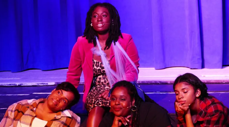 Quattro studentesse della Oakwood Friends School recitano su un palco davanti a un sipario blu.