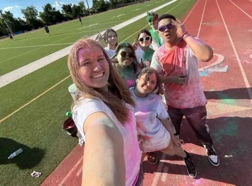 Selfie de un grupo de alumnos cubiertos de polvos de colores en la pista de atletismo