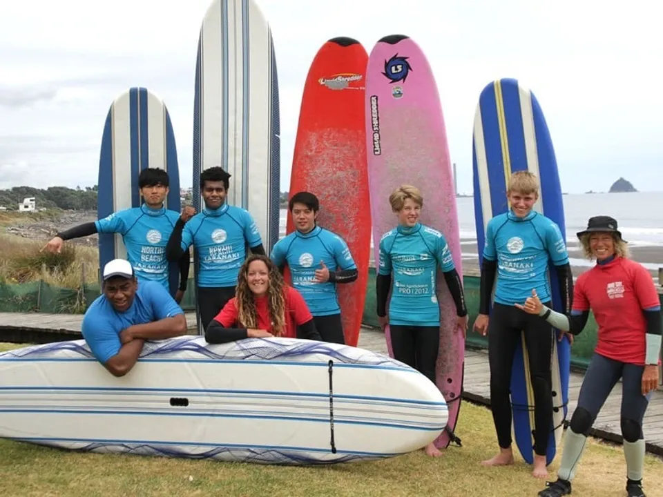 Studenti della New Plymouth Boys' High School posano davanti a tavole da surf e a un veicolo con le montagne sullo sfondo.