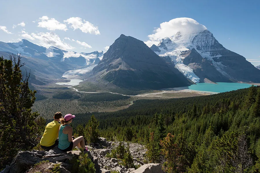 Dos personas están sentadas en una roca y disfrutan del paisaje montañoso con lago cerca de la Valemount Secondary School.