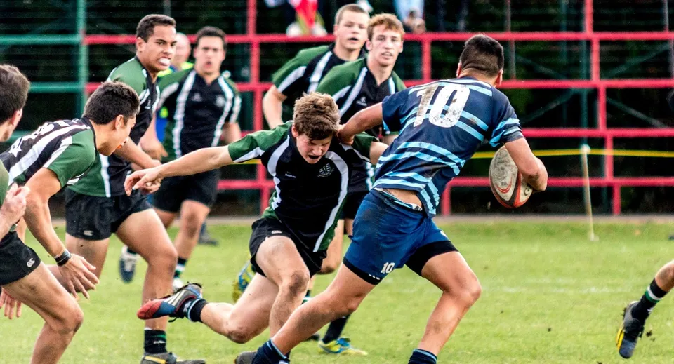 Studenti dell'Otumoetai College giocano una partita di rugby intensa su un campo da gioco circondato da una recinzione.