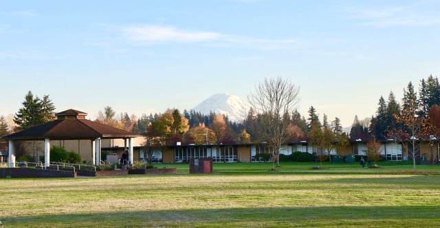 Auf dem Gelände der Auburn Adventist Academy ist ein Pavillon auf einer Wiesenfläche mit Bäumen und schneebedecktem Berg im Hintergrund zu sehen.