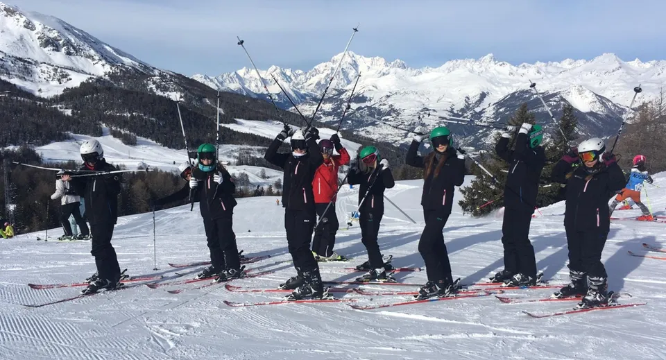Un gruppo di studenti della Ferndown Upper School si trova su un pendio innevato con le montagne sullo sfondo.