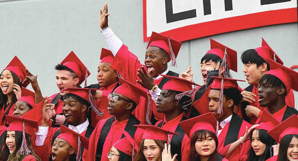 Un gruppo di diplomati della Life Prep Academy in toga rossa sta davanti a una grande scritta Life e festeggia il proprio diploma.