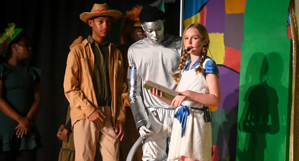 Studenti della Trinity Christian Academy posano in variopinti costumi teatrali davanti a uno sfondo astratto e colorato.
