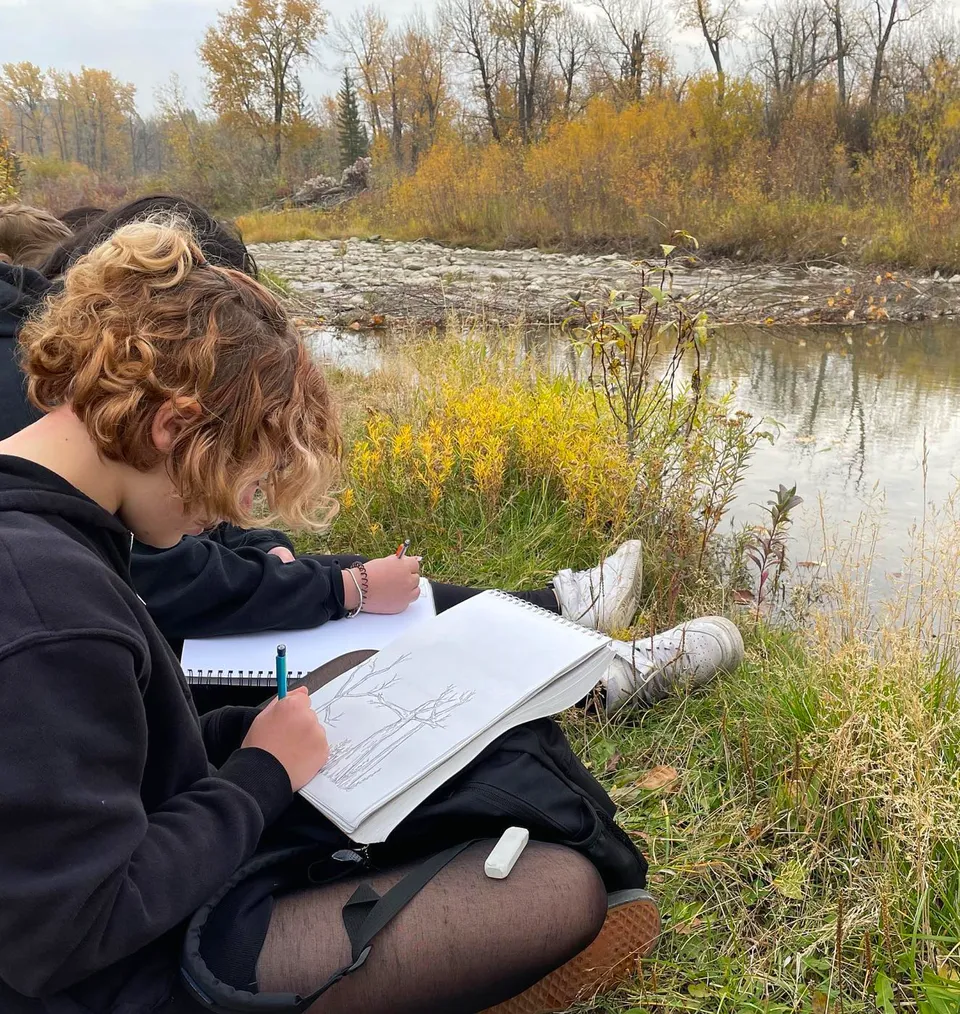 Una persona scrive su un taccuino vicino a un laghetto immerso nella natura nel campus della Henry Wise Wood High School.