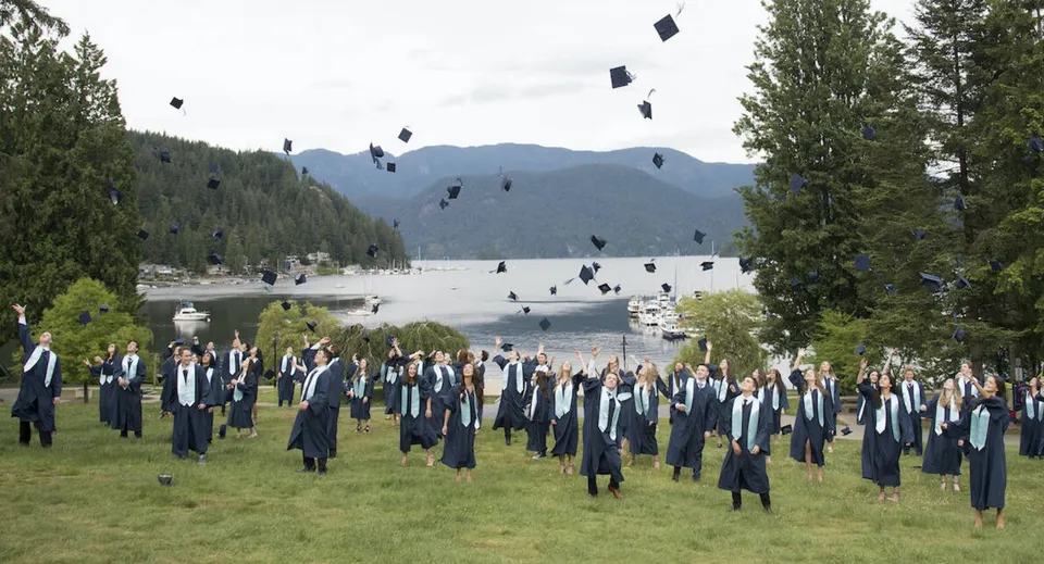 Un grande gruppo di diplomati della Seycove Secondary School si trova su un campo con montagne e un lago sullo sfondo.