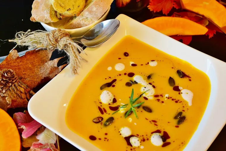 Kürbissuppe mit Kürbiskernen und Kräutern in einer weißen Schale, daneben Brot