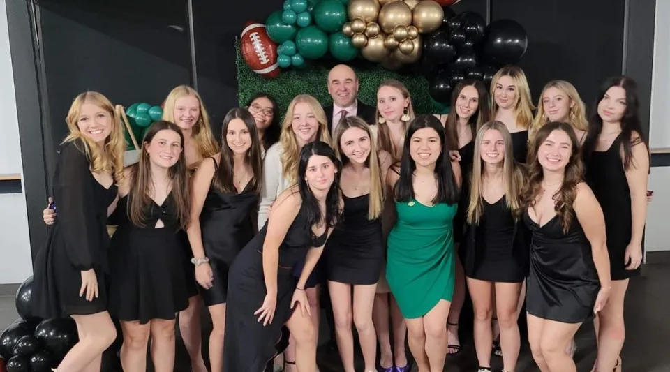 Un gruppo di giovani donne in abiti formali posa davanti a palloncini colorati nell'area della St. Benedict Catholic Secondary School.