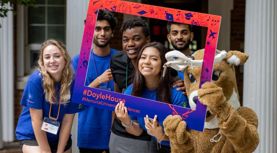 Un gruppo di studenti sorridenti posa davanti a una cornice colorata con la scritta #DayleHouse nel campus della Memorial University.