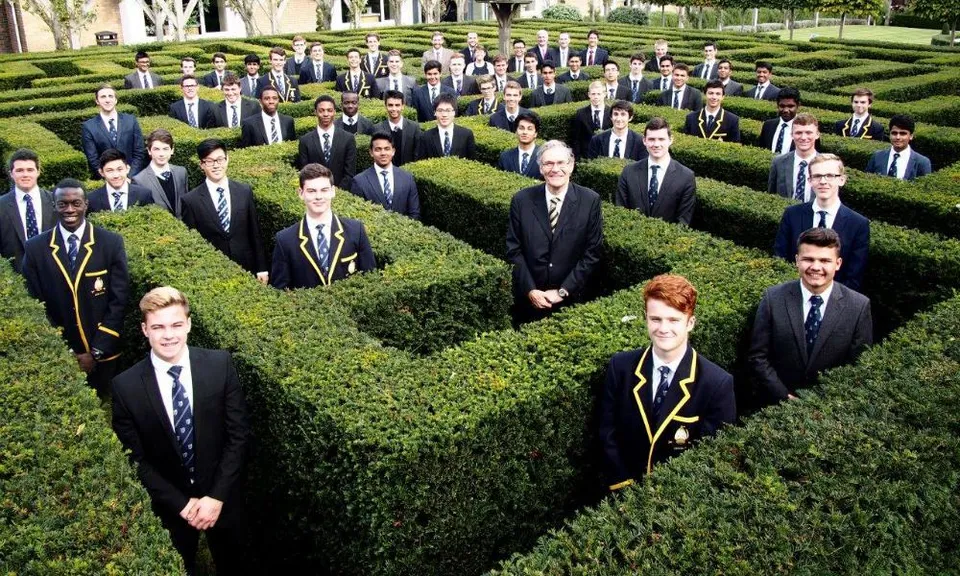 Un gruppo di persone in abiti formali si trova tra siepi ben curate nel campus della Whitgift School.