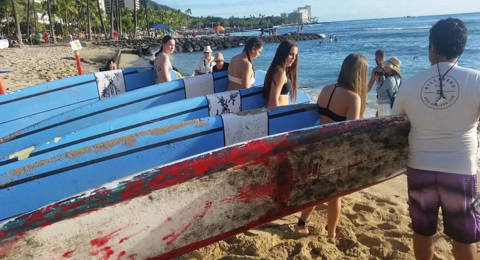 Un gruppo di studenti della Robina State High School si trova sulla spiaggia accanto a tavole da surf colorate con lo skyline della città sullo sfondo.