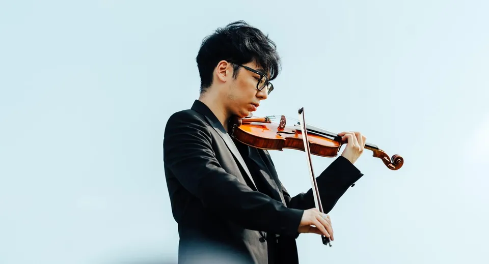 Un giovane ragazzo suona il violino davanti a uno sfondo blu nel campus del St. Mary’s College.