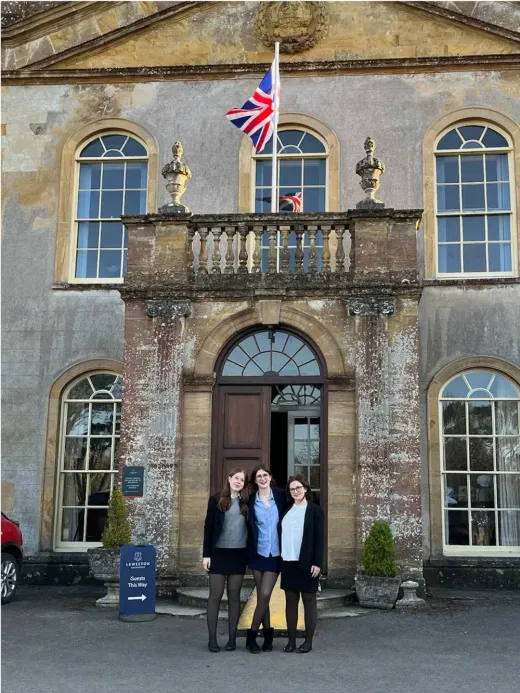 Drei Schülerinnen in Uniform vor einer englischen Schule mit britischer Flagge
