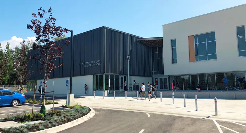 Si vede il moderno edificio a più piani della R.E. Mountain Secondary School con facciata scura e pavimentazione esterna circostante.