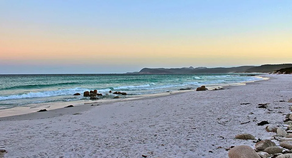 Una spiaggia tranquilla con onde e rocce sotto il cielo al cambio di luce nei dintorni del Kawana Waters State College.