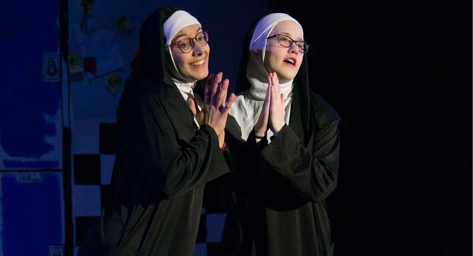 Due studentesse della Freedom Preparatory Academy indossano abiti religiosi tradizionali su uno sfondo blu.