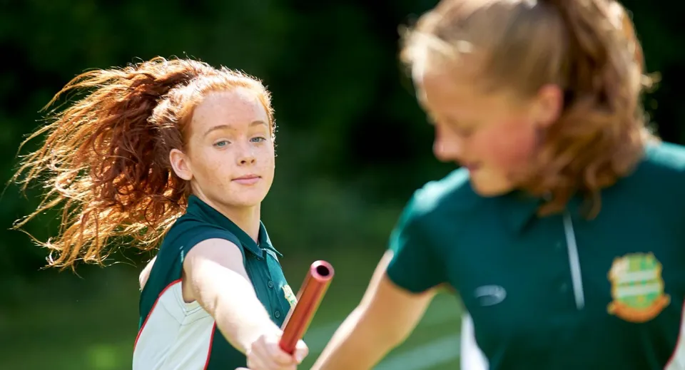 Due studentesse della Farringtons School chiacchierano all'aperto con uno sfondo verde.