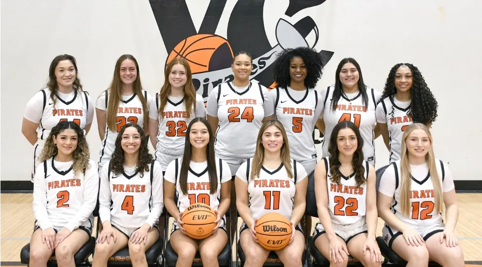 Un gruppo di giovani studentesse in maglia da basket posa davanti a un muro con un grande logo di basket al Ventura County Community College District.