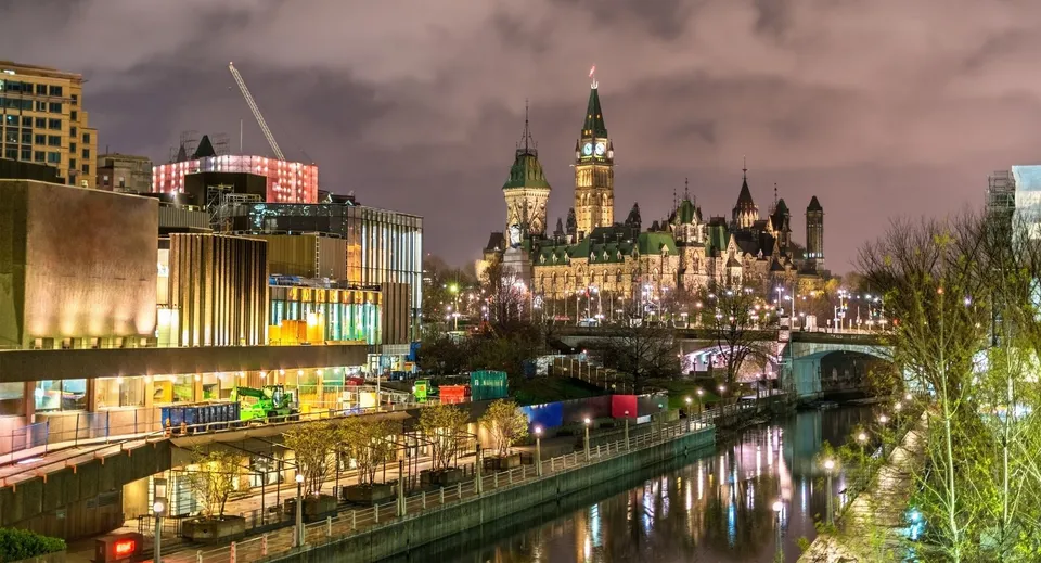 Gli edifici illuminati del Parlamento di Ottawa di notte con il canale Rideau in primo piano.