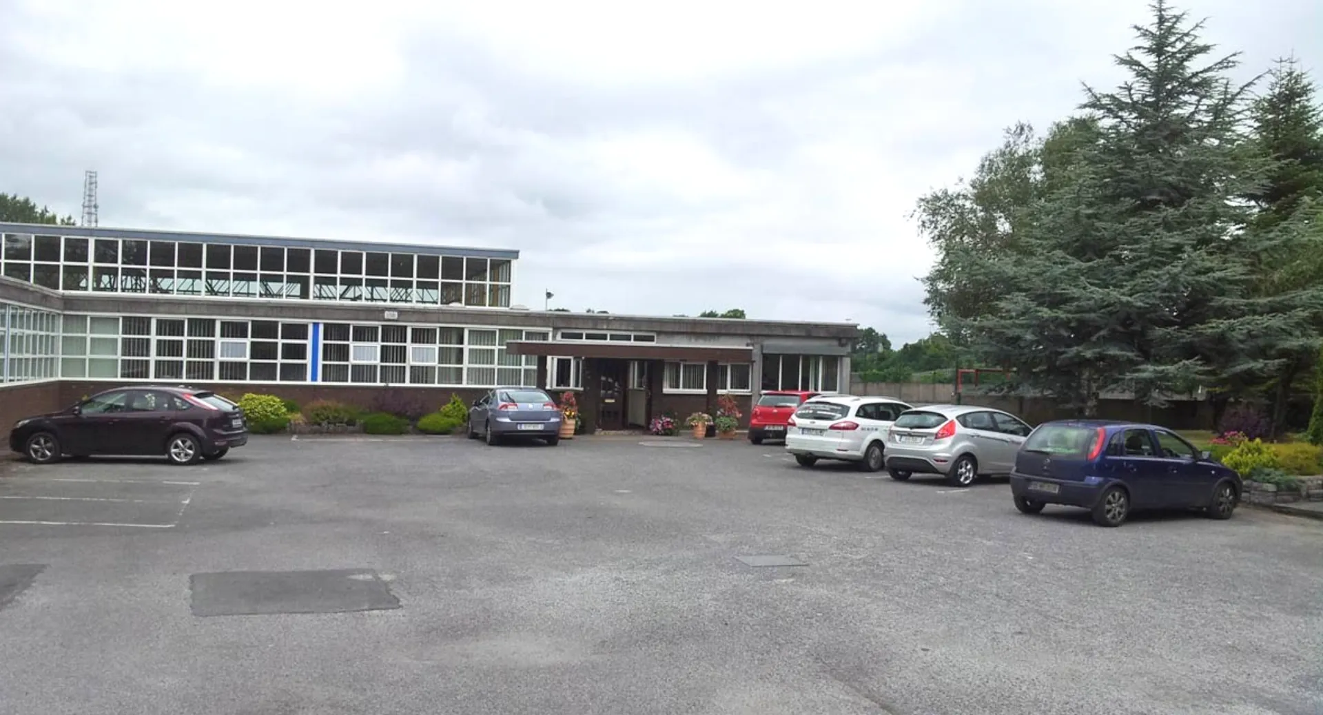 Edificio a più piani del Marist College con parcheggio e alberi sotto un cielo nuvoloso.