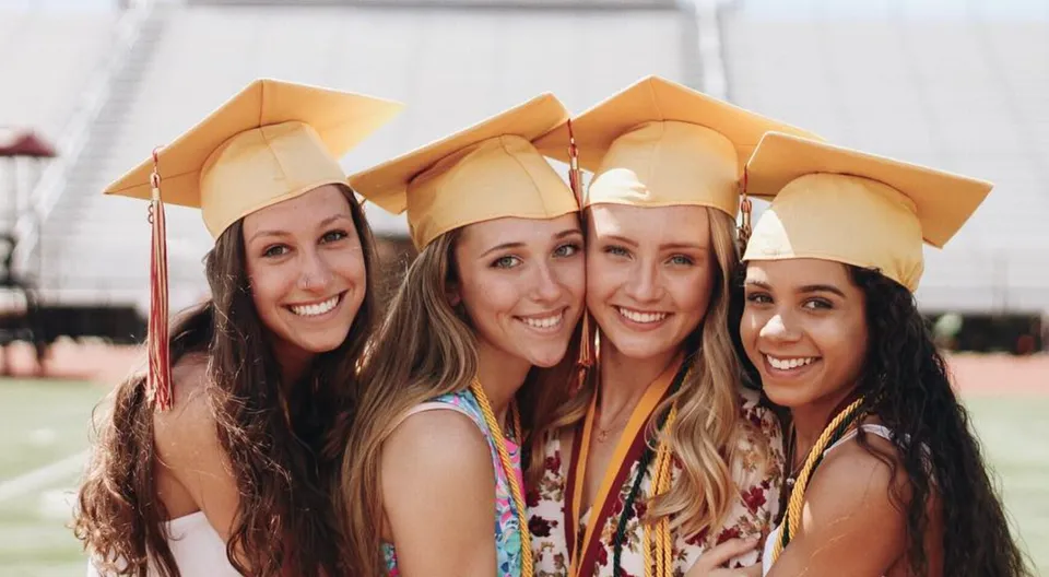 Quattro studentesse in toga da diploma si trovano insieme all'aperto nel campus della Thornton Academy.