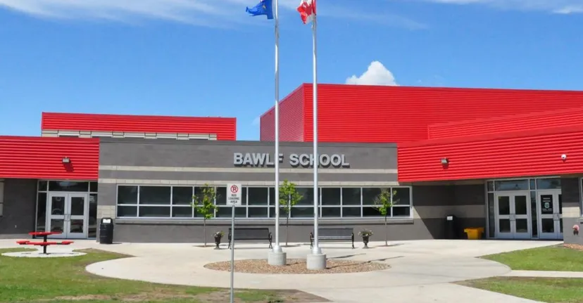 Il moderno edificio scolastico rosso della Bawlf School con la scritta del nome sulla facciata sotto un cielo blu con bandiere al vento.