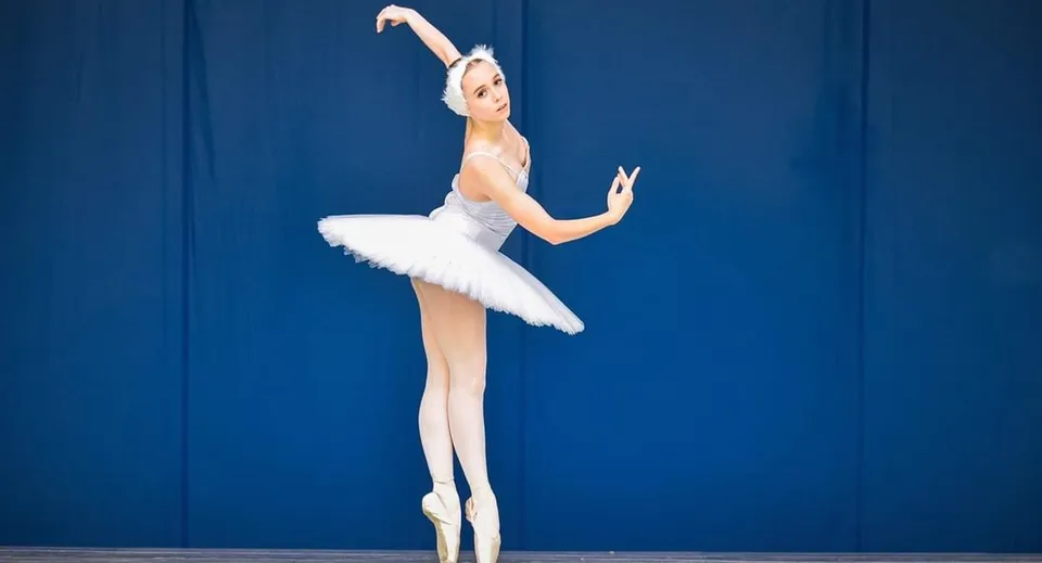 Una ballerina esegue una piroetta durante una lezione di danza al Maine Central Institute, su uno sfondo blu.