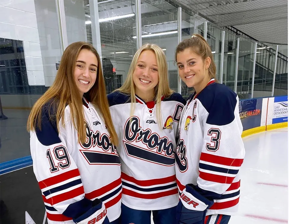 Tre studentesse della Orono High School in maglie da hockey sulla pista di ghiaccio nella palestra.