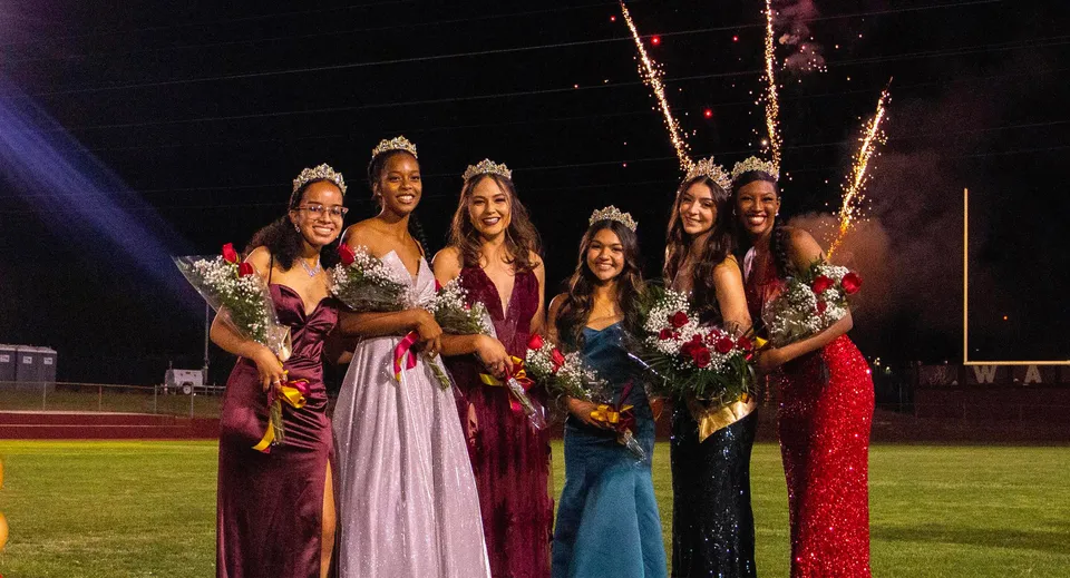 Studentesse della Bishop Alemany High School in abiti eleganti con bouquet di fiori in piedi sul campo sportivo mentre sullo sfondo si vedono fuochi d'artificio.