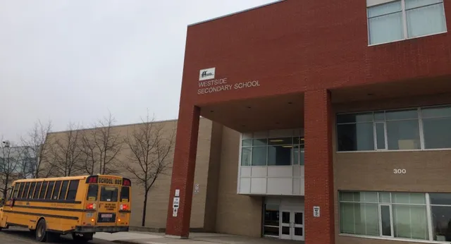 Si vede l'edificio in mattoni della Westside Secondary School con uno scuolabus giallo davanti.