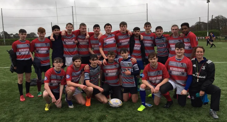 Un gruppo di giovani calciatori in divisa rossa e grigia posa sul campo sportivo del Mullingar Community College.