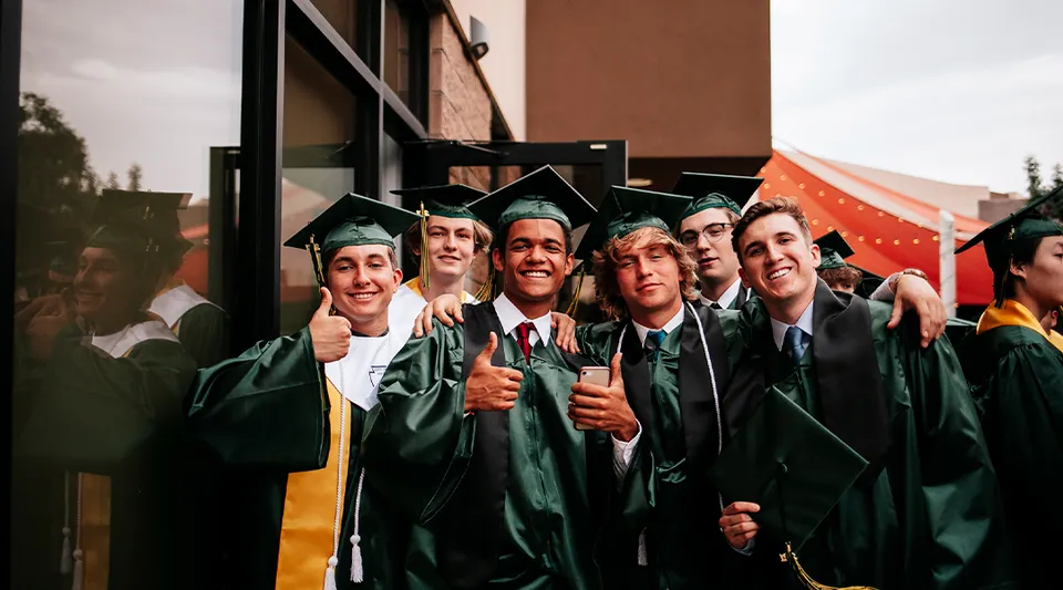Un gruppo di diplomati in toga verde è davanti a un edificio e festeggia il proprio diploma alle Gilbert Christian Schools.