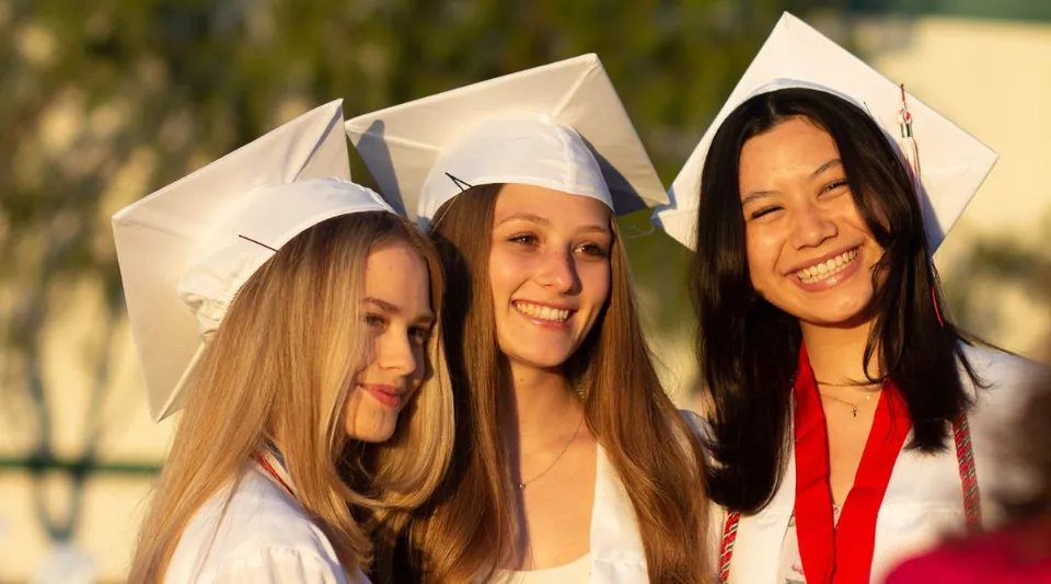Tre studentesse della Flintridge Sacred Heart Academy in abito da diploma stanno insieme all'aperto davanti a uno sfondo naturale.