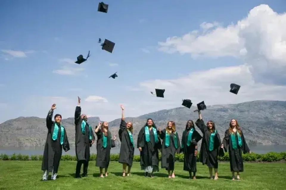 Un gruppo di diplomati della Unisus School lancia in aria i propri tocchi davanti a un lago e alle montagne.