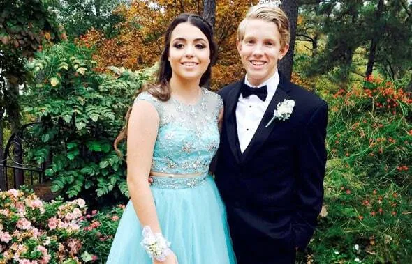 Pareja de estudiantes con vestido de gala azul y esmoquin negro posa en un jardín