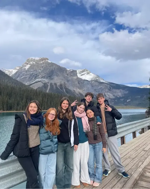 Sette studenti in posa su un pontile davanti a un lago e montagne innevate durante una gita in Canada