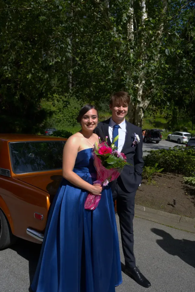 Coppia di studenti in abiti eleganti con bouquet accanto a un'auto d'epoca in Canada