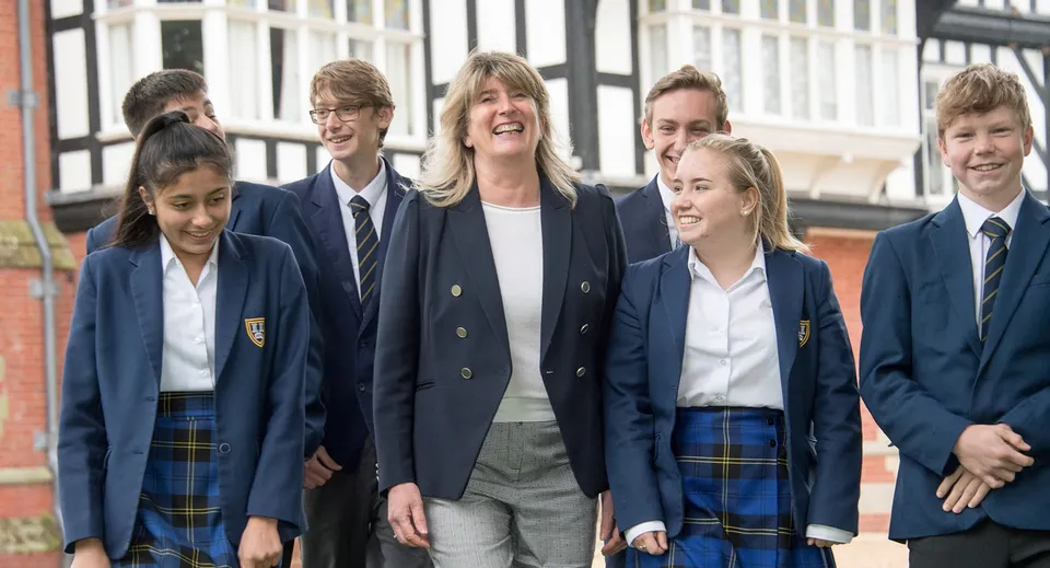 Un gruppo di studenti e studentesse sta sorridente davanti a un edificio con grandi finestre nel campus della Bedstone School.