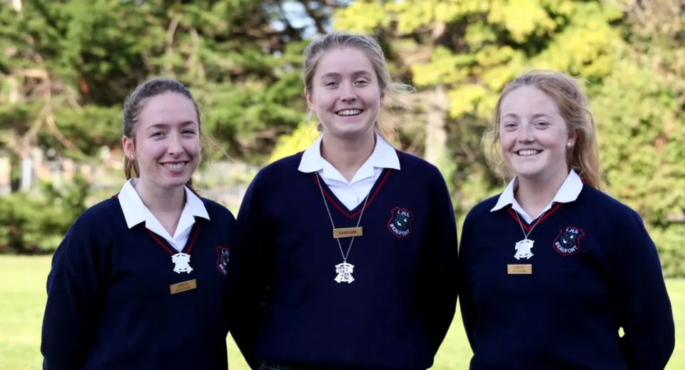 Tre studentesse della Loreto High School Beaufort sorridono in un'area verde con alberi simile a un parco.