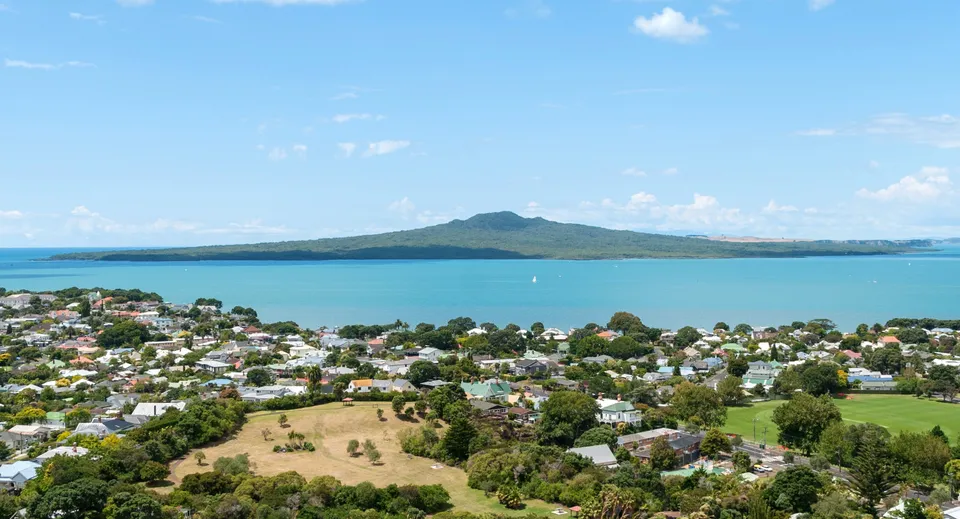 Vista sul paesaggio costiero con una baia turchese e montagne sullo sfondo vicino al Rangitoto College.