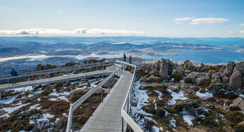 Studenti del Rosny College camminano su una passerella di legno attraverso un paesaggio montano innevato verso un punto panoramico.